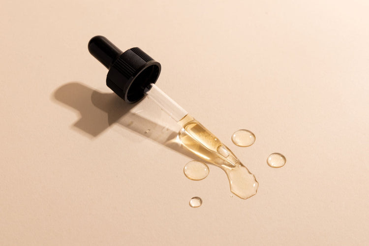 Black dropper laid on a beige surface, golden serum pooling from the pipette to show peptide consistency.