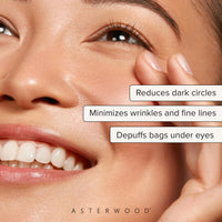 Close-up of a smiling woman holding skin at the outer eye with callouts: reduces dark circles, minimizes wrinkles and fine lines, depuffs bags under eyes.