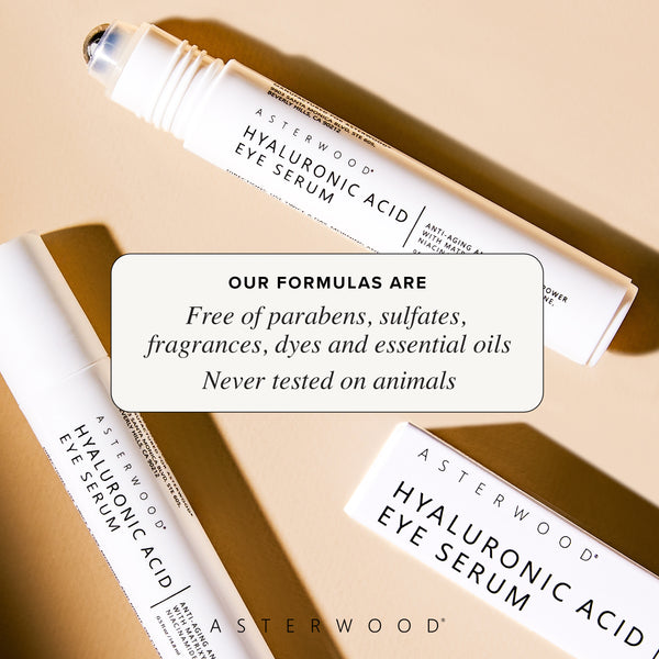 Two Hyaluronic Acid Eye Serum pens crossed on a tan surface with callout that formulas are free of parabens, sulfates, fragrances, dyes, essential oils, cruelty-free.