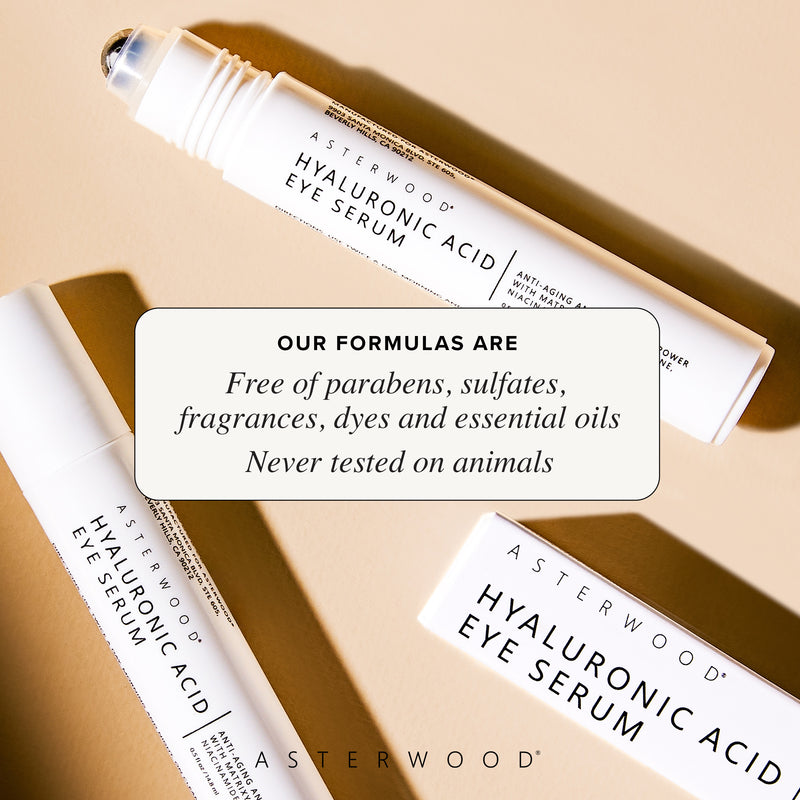 Two Hyaluronic Acid Eye Serum pens crossed on a tan surface with callout that formulas are free of parabens, sulfates, fragrances, dyes, essential oils, cruelty-free.
