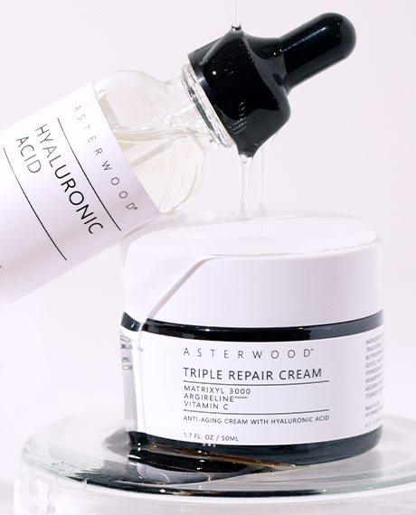 Asterwood Hyaluronic Acid serum dropper poured over the open Triple Repair Cream jar, clear serum drizzling onto a glass dish.