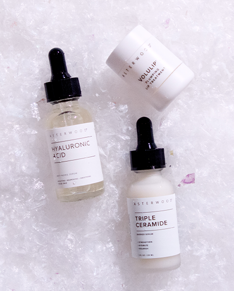 Asterwood Hyaluronic Acid Serum, Triple Ceramide Barrier Serum, and Volulip Plumping Lip Treatment arranged on a frosty white background.