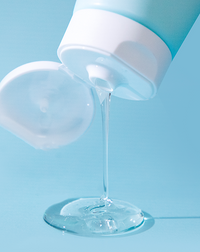 Clear gel cleanser streaming from the Asterwood tube onto a blue surface, showing the lightweight liquid texture.