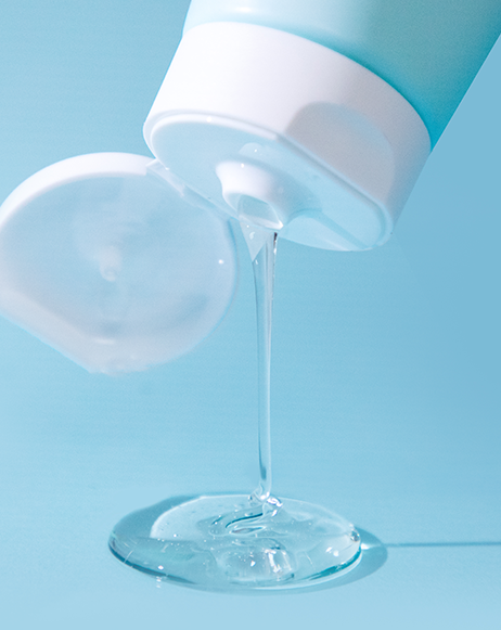Clear gel cleanser streaming from the Asterwood tube onto a blue surface, showing the lightweight liquid texture.