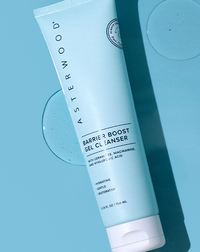 Top-down shot of Asterwood Barrier Boost Gel Cleanser tube on blue background with two clear gel circles, showing the ceramide formula.