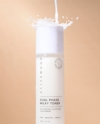 Asterwood Dual Phase Milky Toner bottle on tan background with milky liquid splashing out the top, showing the creamy texture.