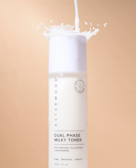 Asterwood Dual Phase Milky Toner bottle on tan background with milky liquid splashing out the top, showing the creamy texture.