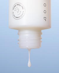 Close-up of the Dual Phase Milky Toner unscrewed cap with a milky droplet falling from the threaded opening against a soft blue background.
