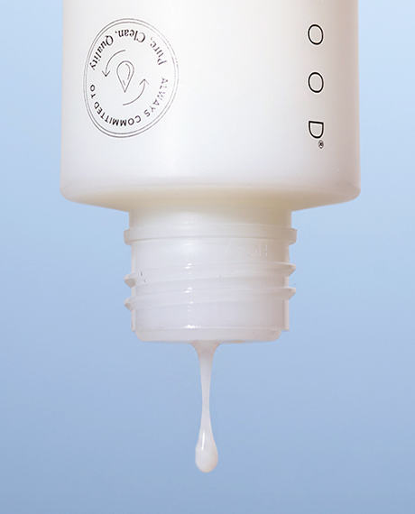 Close-up of the Dual Phase Milky Toner unscrewed cap with a milky droplet falling from the threaded opening against a soft blue background.