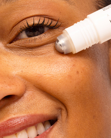 Smiling woman rolling the Asterwood Hyaluronic Acid Eye Serum metal applicator under her eye.
