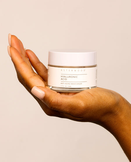Hand cradling the Asterwood Hyaluronic Acid Anti-Aging Moisturizer jar in front of a soft beige background.