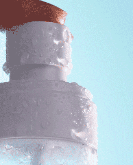 Animated close-up of Asterwood Hypochlorous Acid Facial Mist droplets beading on the frosted bottle against a soft blue background.