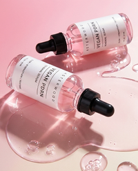 Two Asterwood Vegan PDRN Renewal Serum bottles lying in spilled pink serum on a pink background.