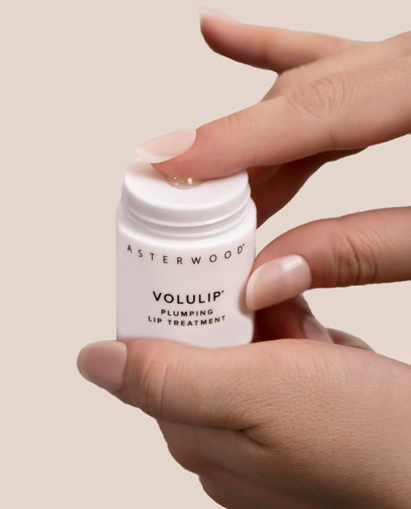Hands holding the open Asterwood Volulip Plumping Lip Treatment, a glossy bead of balm at the twist-up base.